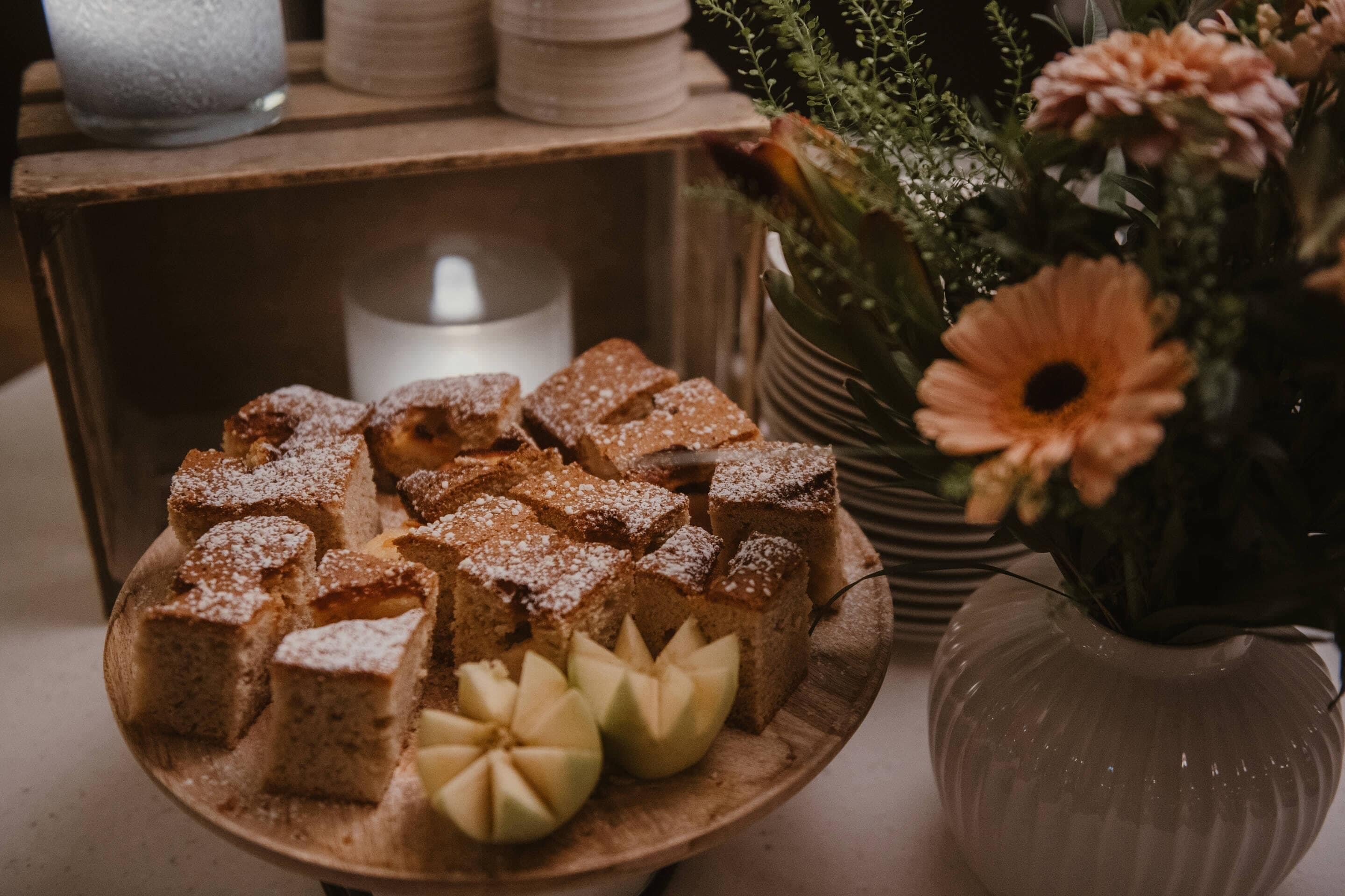 Une planche en bois sur laquelle est disposé un dessert, un vase rempli de fleurs et une bougie.