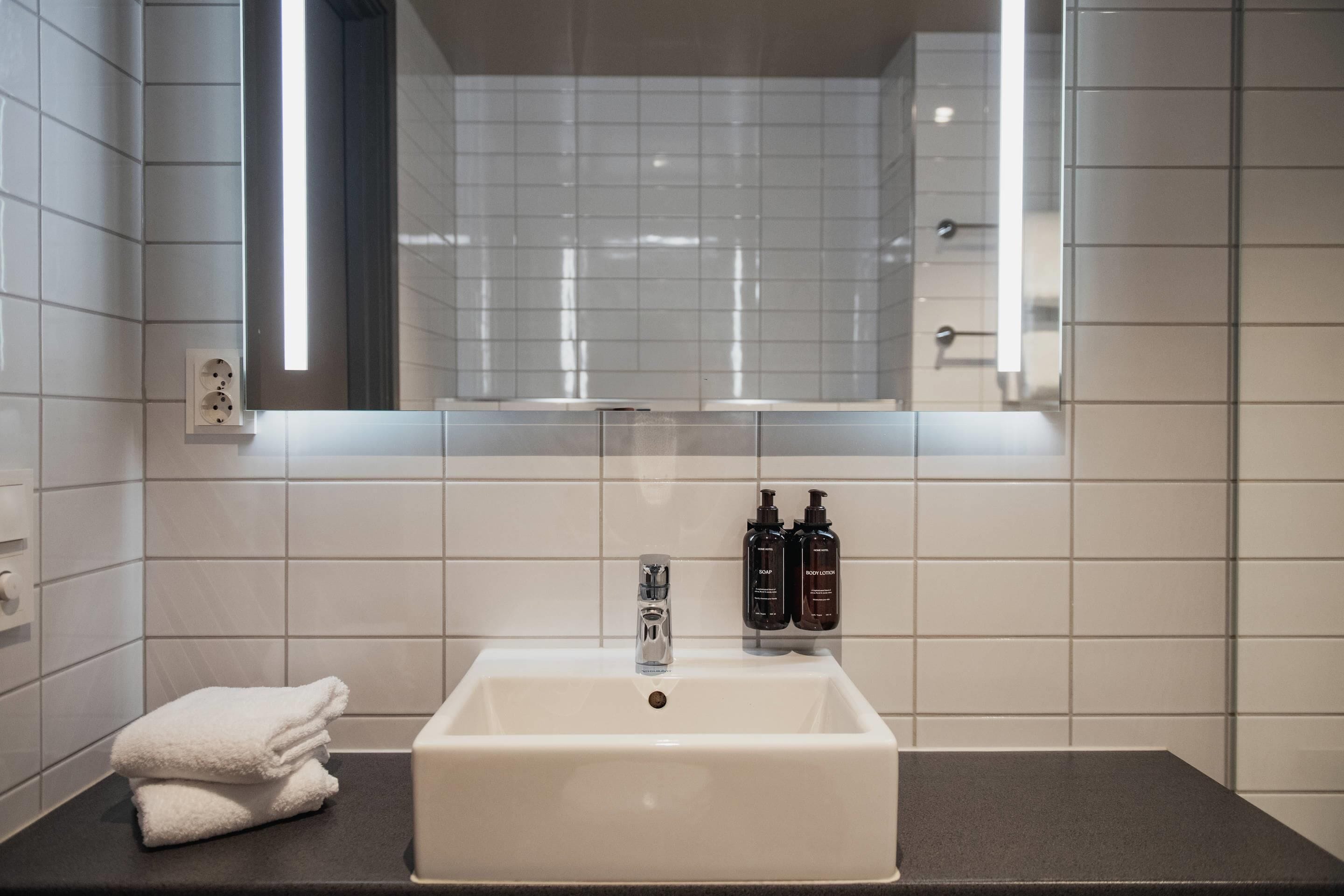 Ein Badezimmer mit einem weißen Waschbecken, einem Spiegel darüber und zwei Shampooflaschen an der Wand.