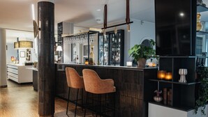 A modern bar area with two bar stools, a large pillar, and a shelf with candles and a plant.