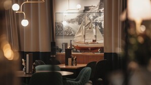 A restaurant interior with a large window displaying a model ship, tables, chairs, and pendant lighting.