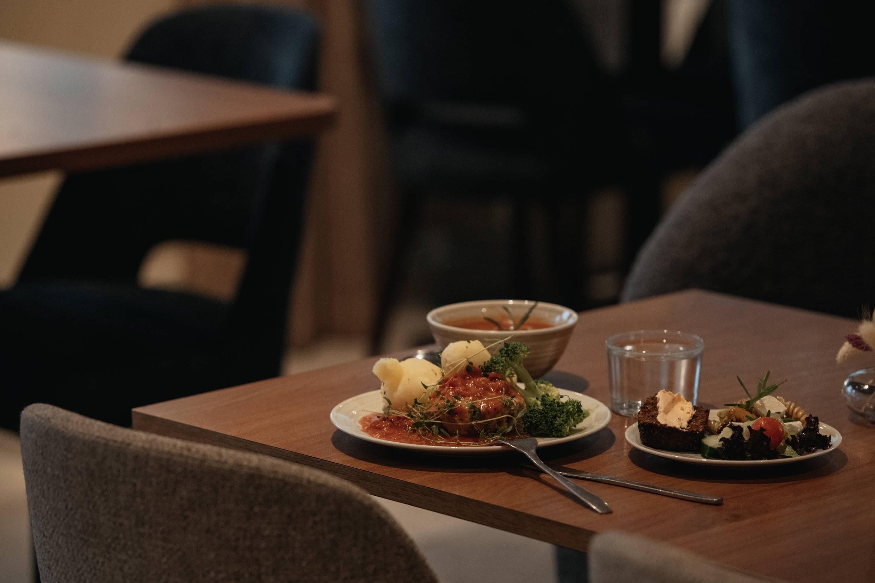A dining table with plates of food, a glass of water, and a bowl of soup.