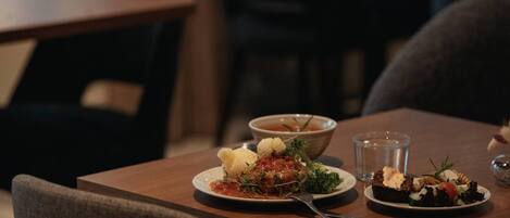 A dining table with plates of food, a glass of water, and a bowl of soup.