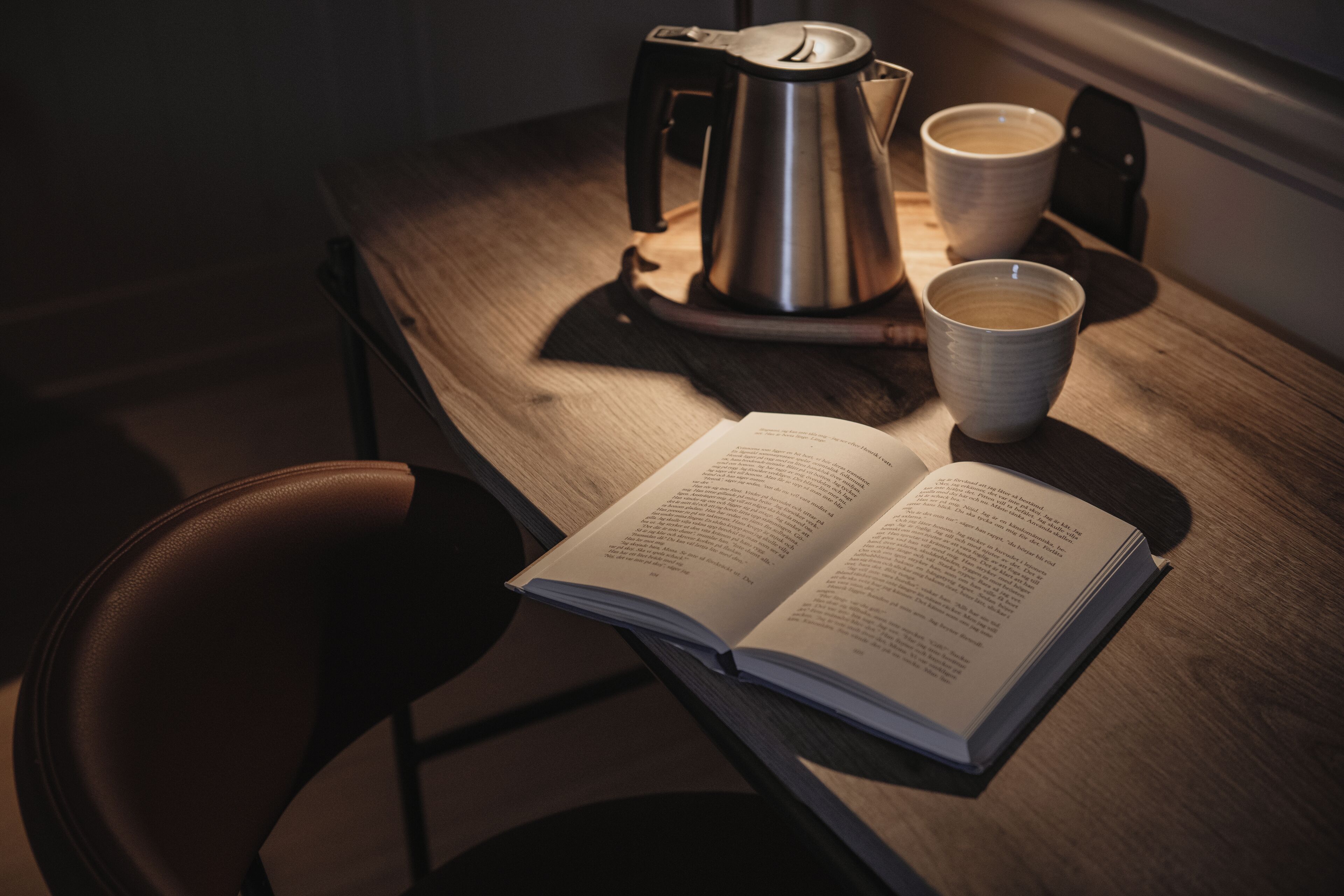 A wooden table with a kettle, two cups, and an open book.