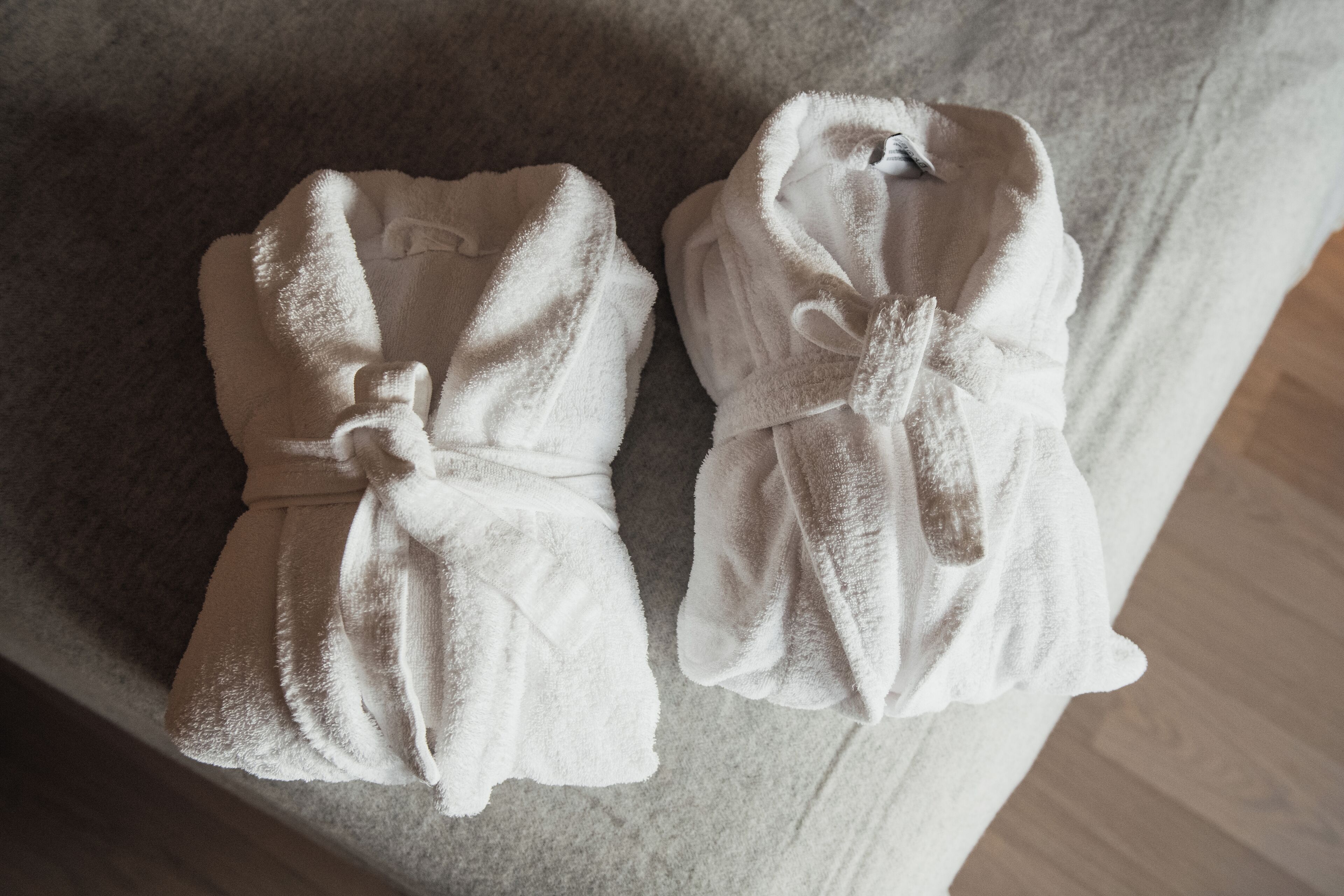 Two white bathrobes with ties on a textured surface.
