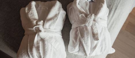 Two white bathrobes with ties on a textured surface.