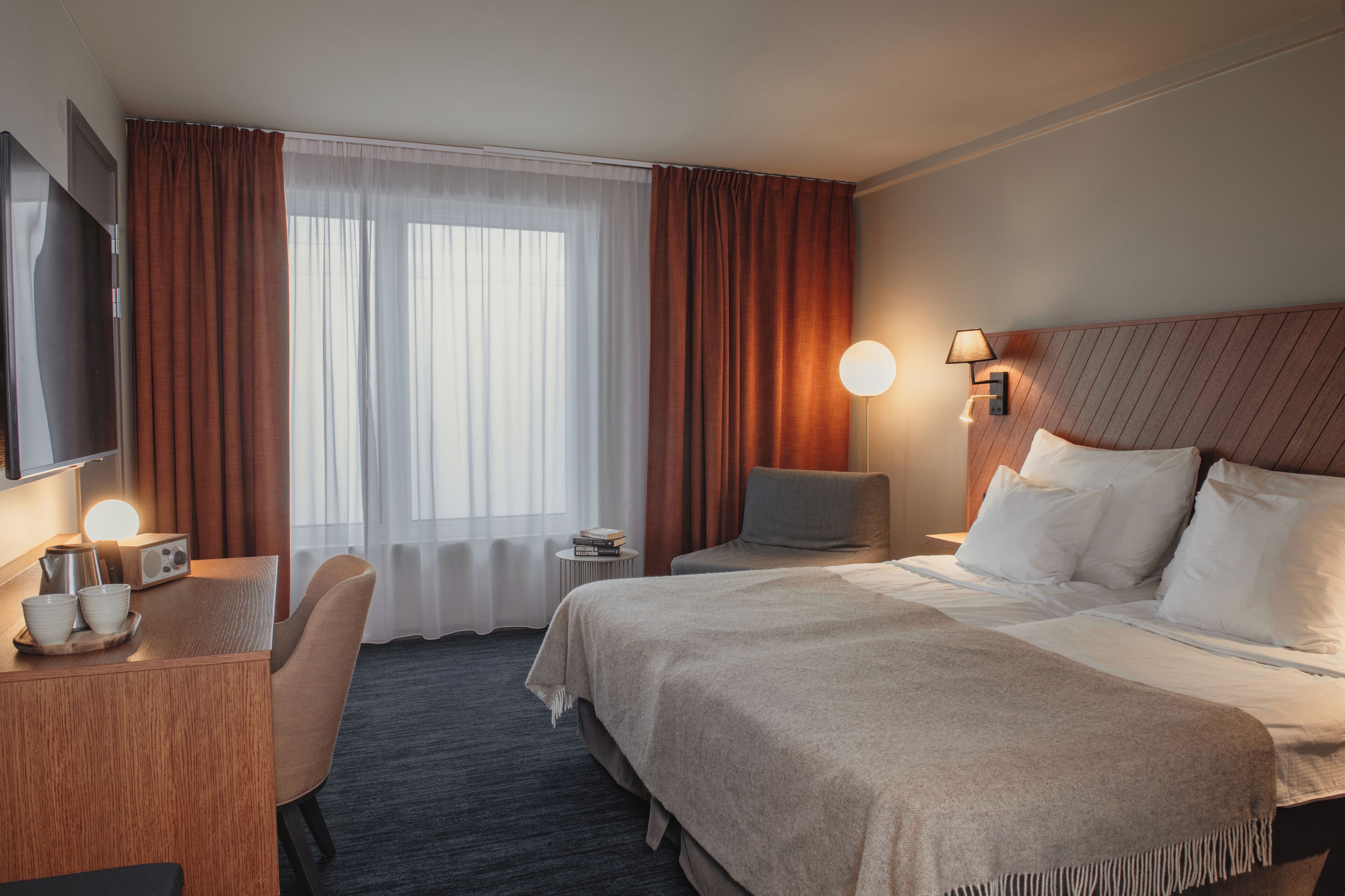 A hotel room with a bed, bedside table, TV, and a desk with a chair.