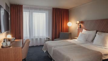 A hotel room with a bed, bedside table, TV, and a desk with a chair.