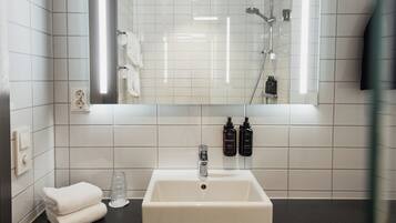 Une salle de bain avec des carreaux blancs, un lavabo, un miroir, un porte-serviettes et deux bouteilles de lotion pour le corps.