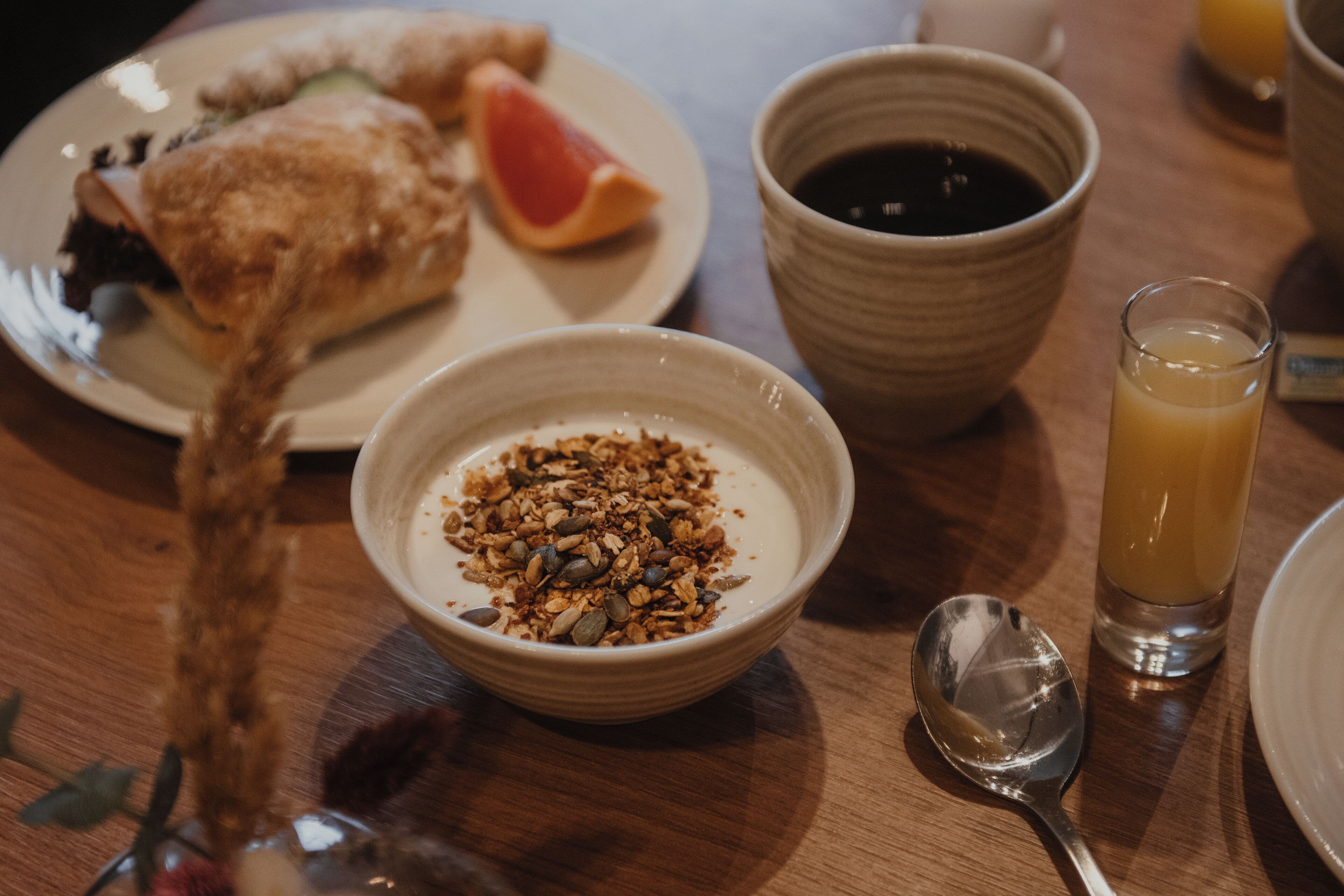 Un desayuno con un plato de comida, un tazón de granola, una taza de café y un vaso de jugo de naranja.
