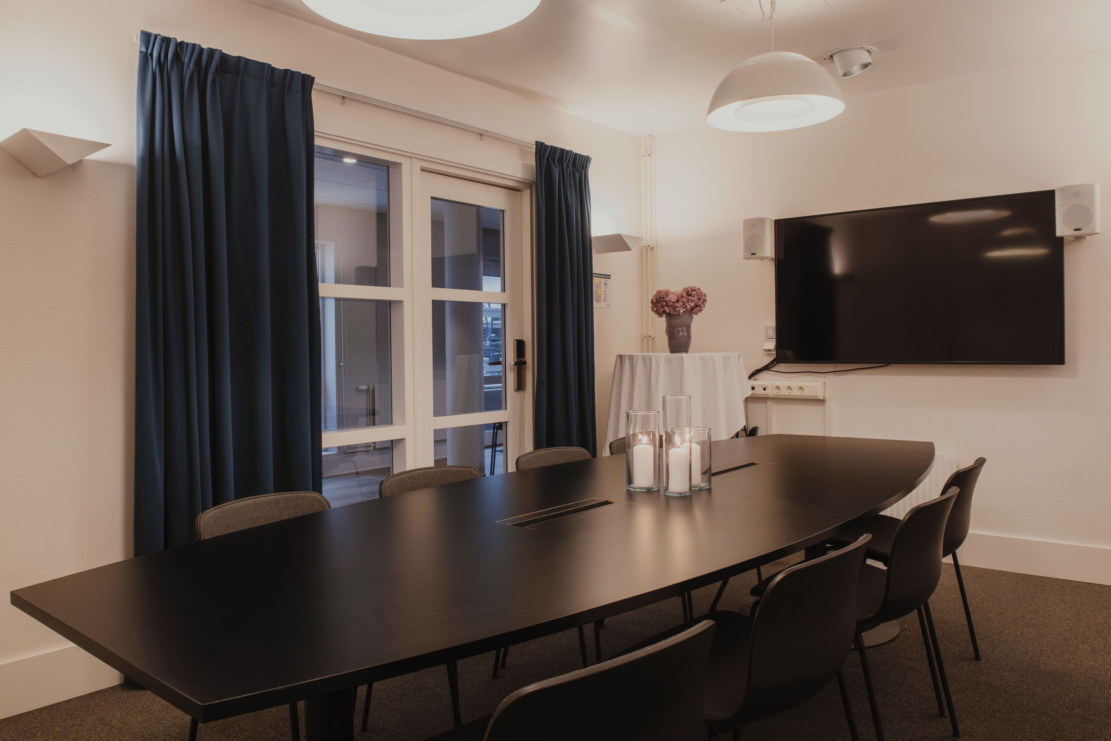 A conference room with a long table, chairs, a TV, and a vase with flowers.