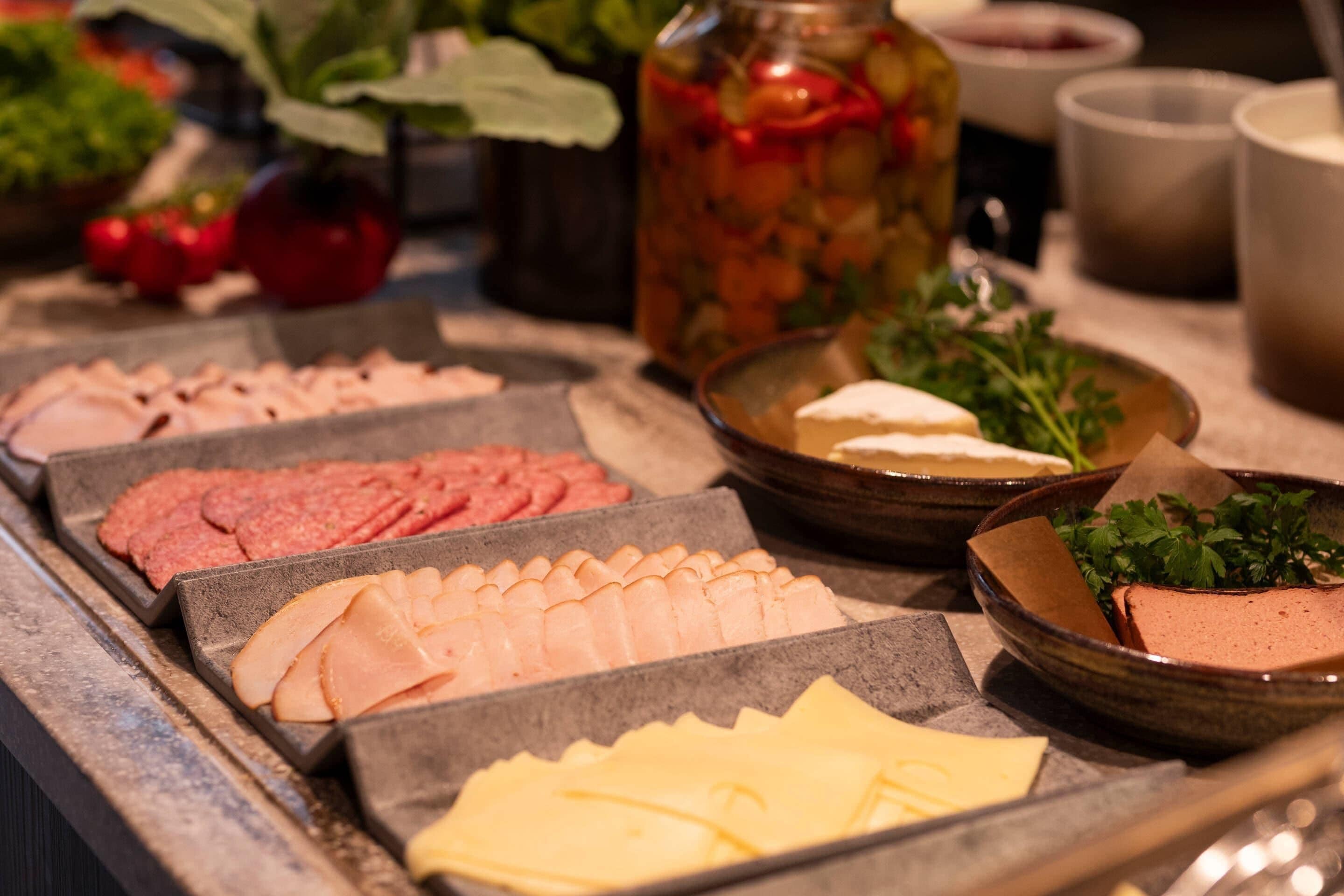 Een ontbijtbuffet met diverse soorten eten, zoals vleesschotels, kazen en een pot augurken.