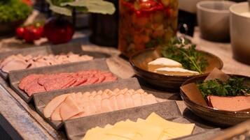 Een ontbijtbuffet met diverse soorten eten, zoals vleesschotels, kazen en een pot augurken.