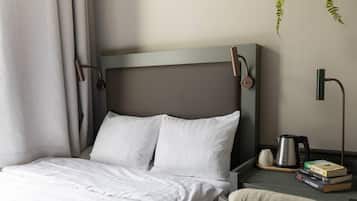 A neatly made bed with white linens, a bedside table with a kettle, books, and a cup.