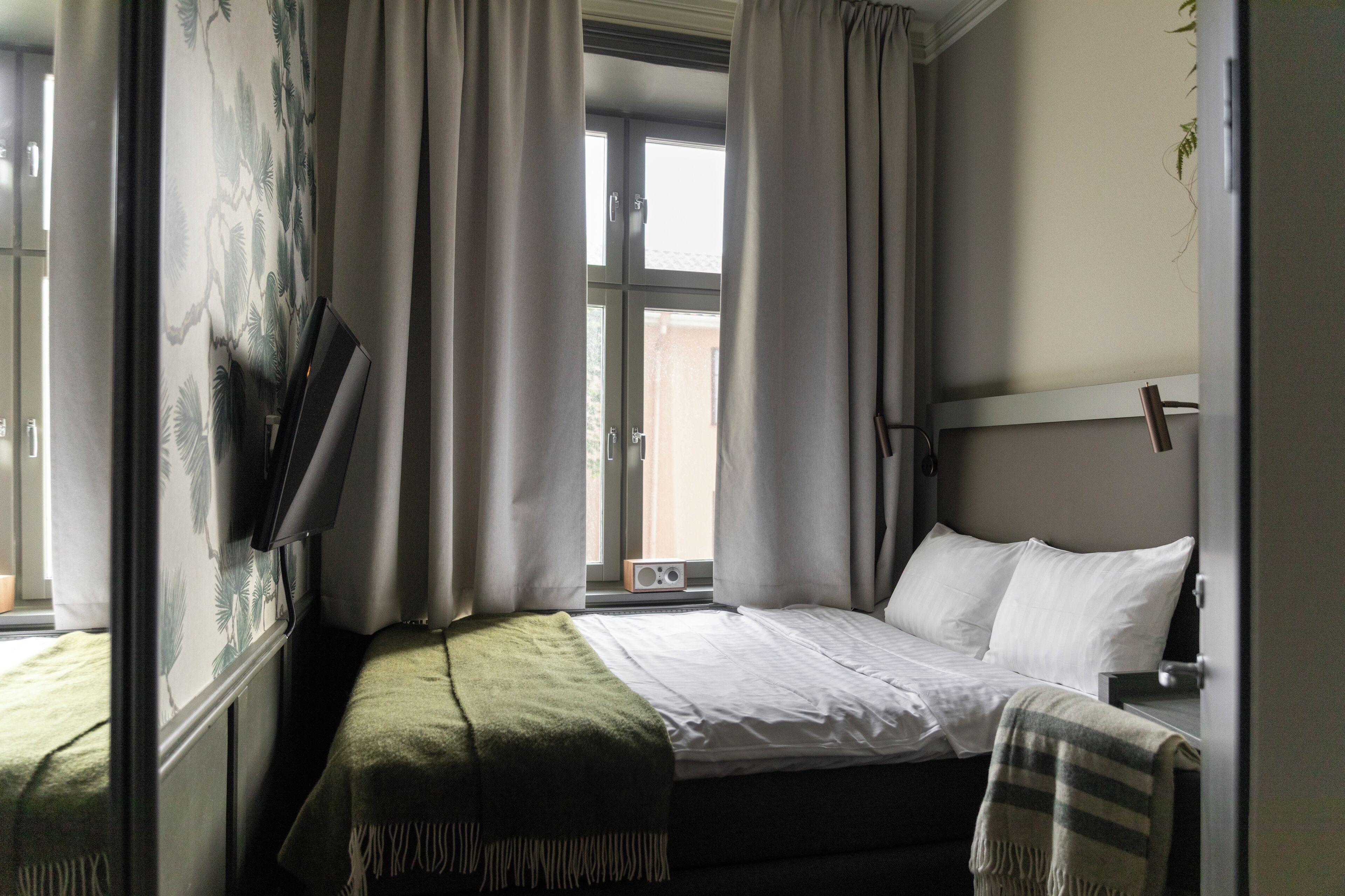 A bedroom with a bed, a TV, and a window with curtains.