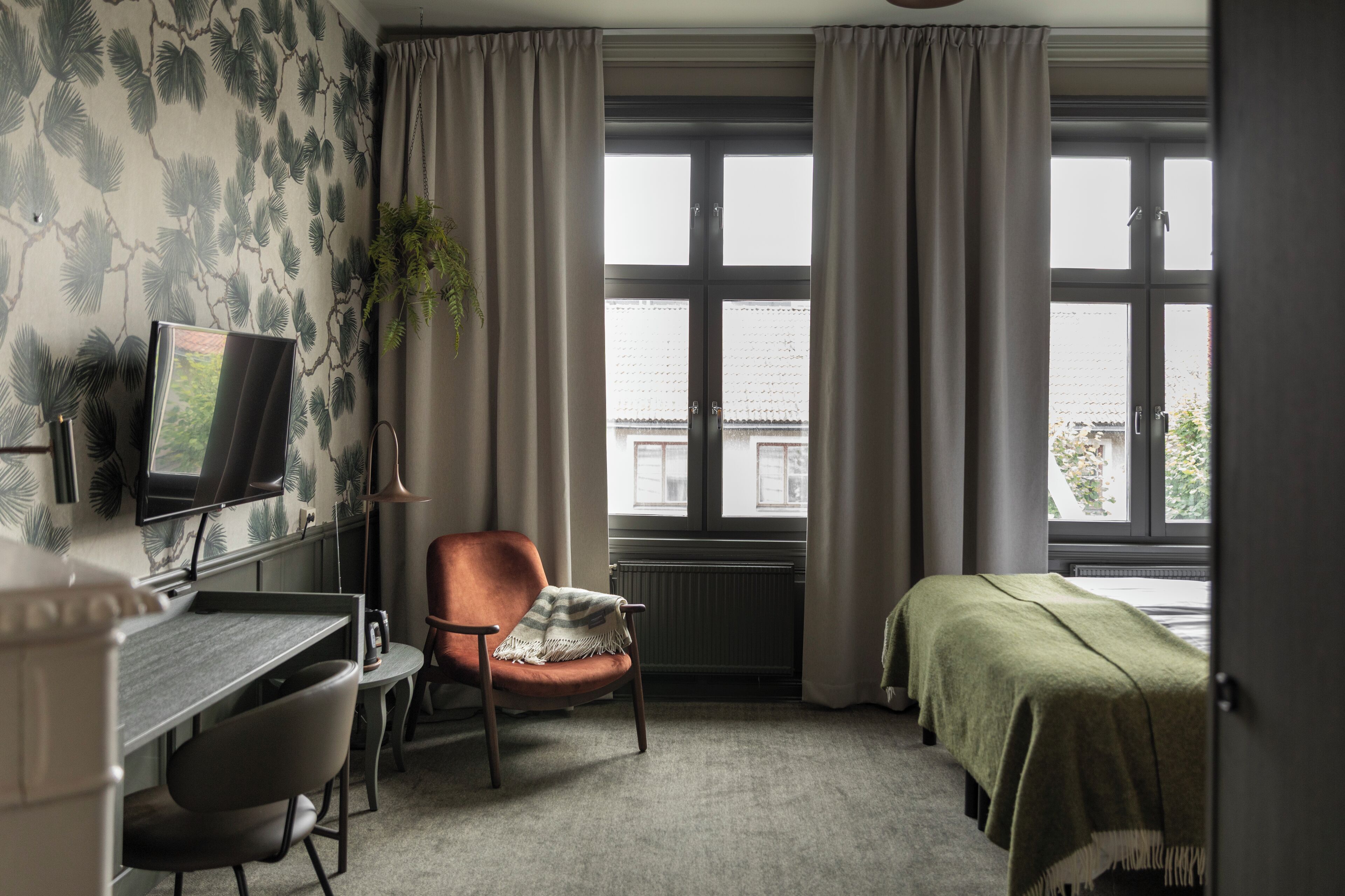 A room with a desk, chair, bed, and large windows.