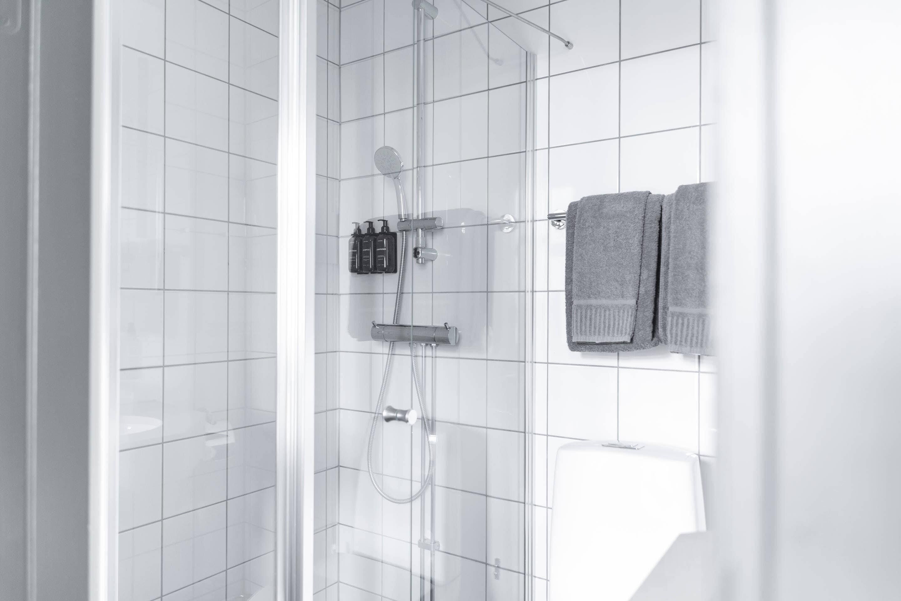 Ein modernes Badezimmer mit weißen Fliesen, einer Duschkabine aus Glas und einem Handtuchhalter mit zwei Handtüchern.