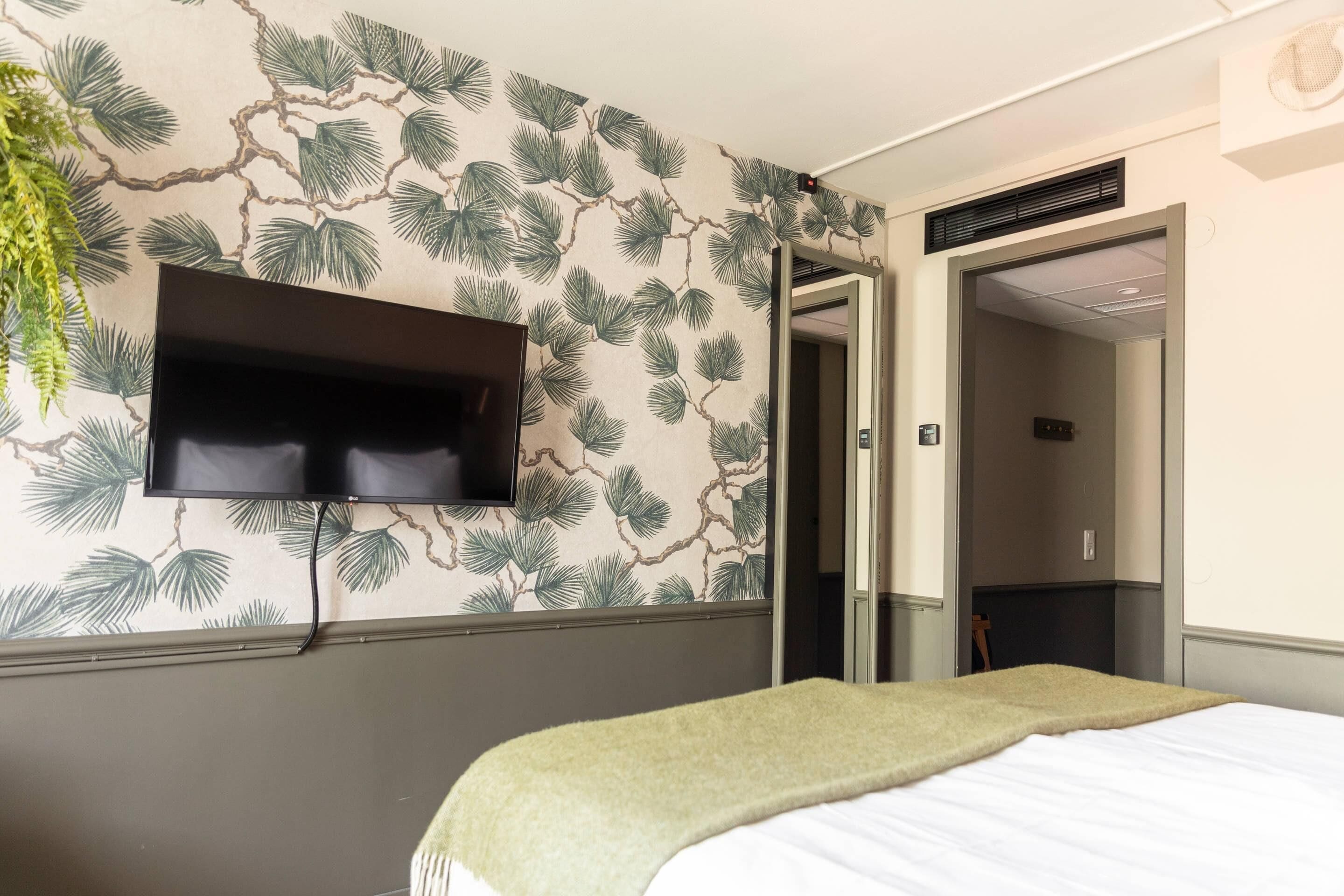 A hotel room with a bed, a mounted TV, and a door leading to another room.