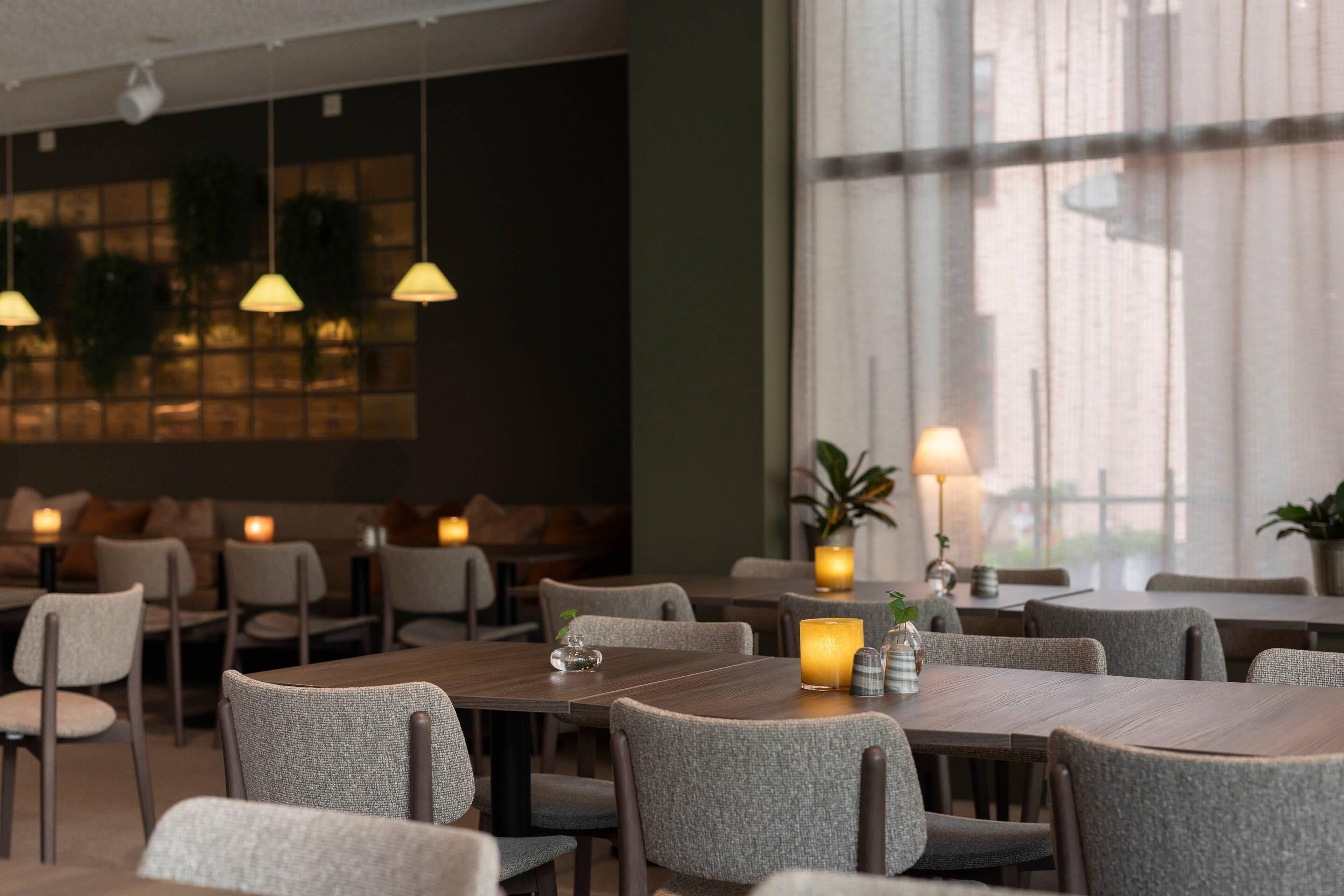A restaurant with multiple tables and chairs, candles, and hanging lights.