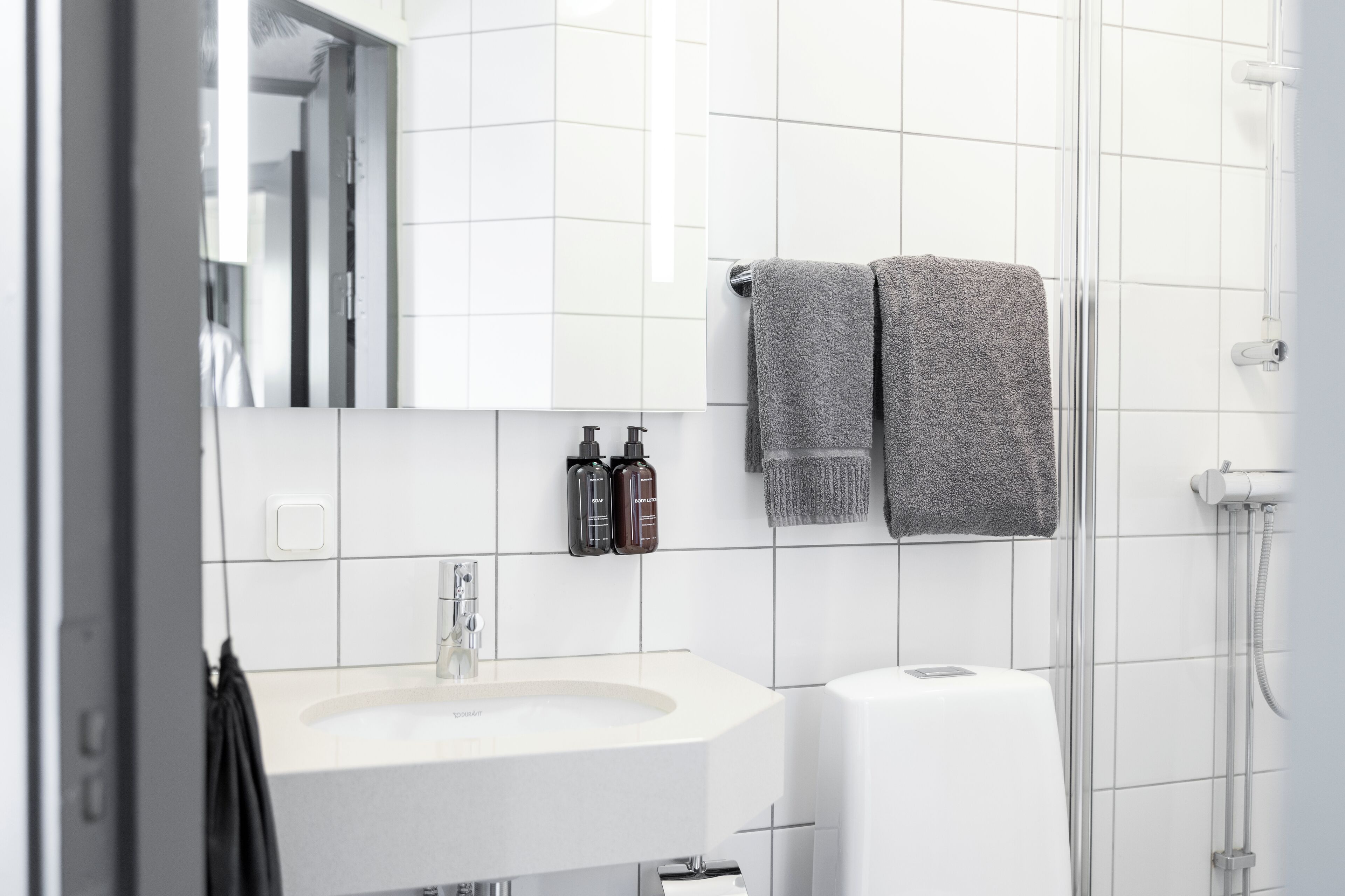 A modern bathroom with a white sink, two bottles of toiletries, and two towels on a rack.