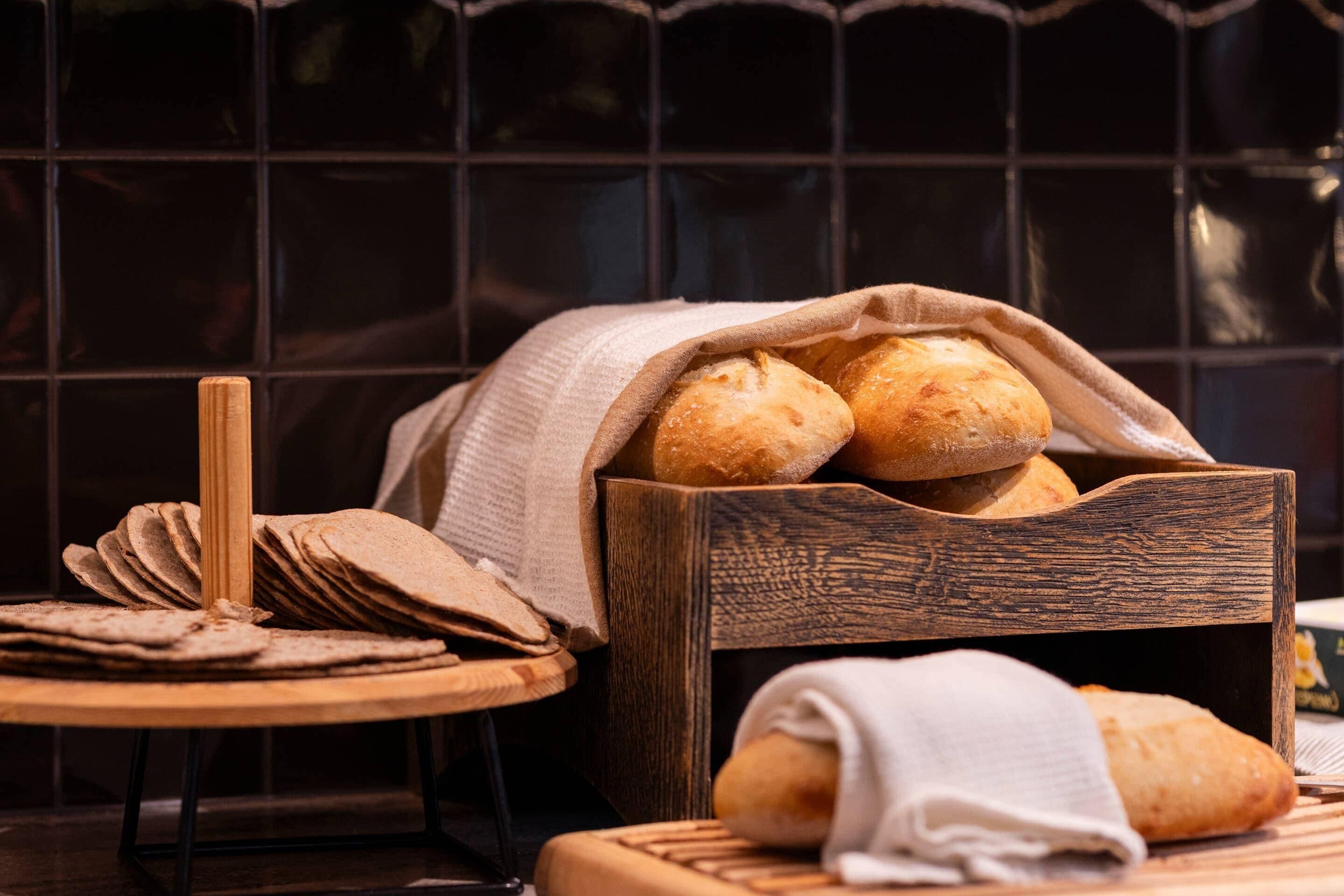 A wooden bread basket with several loaves of bread, a cutting board, and a cloth napkin.