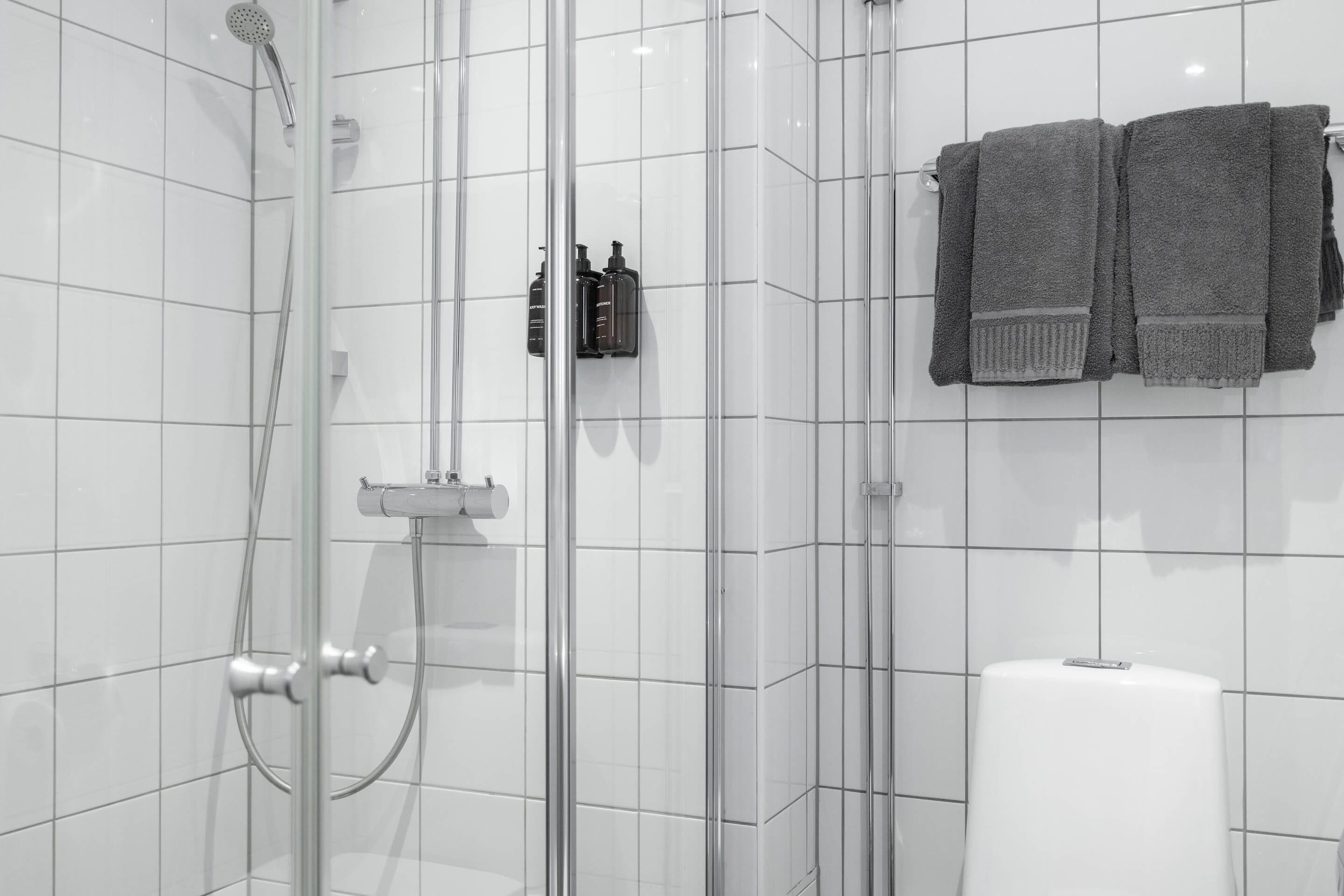 Un baño moderno con ducha envuelta en vidrio, un inodoro y dos toallas colgadas en un perchero.