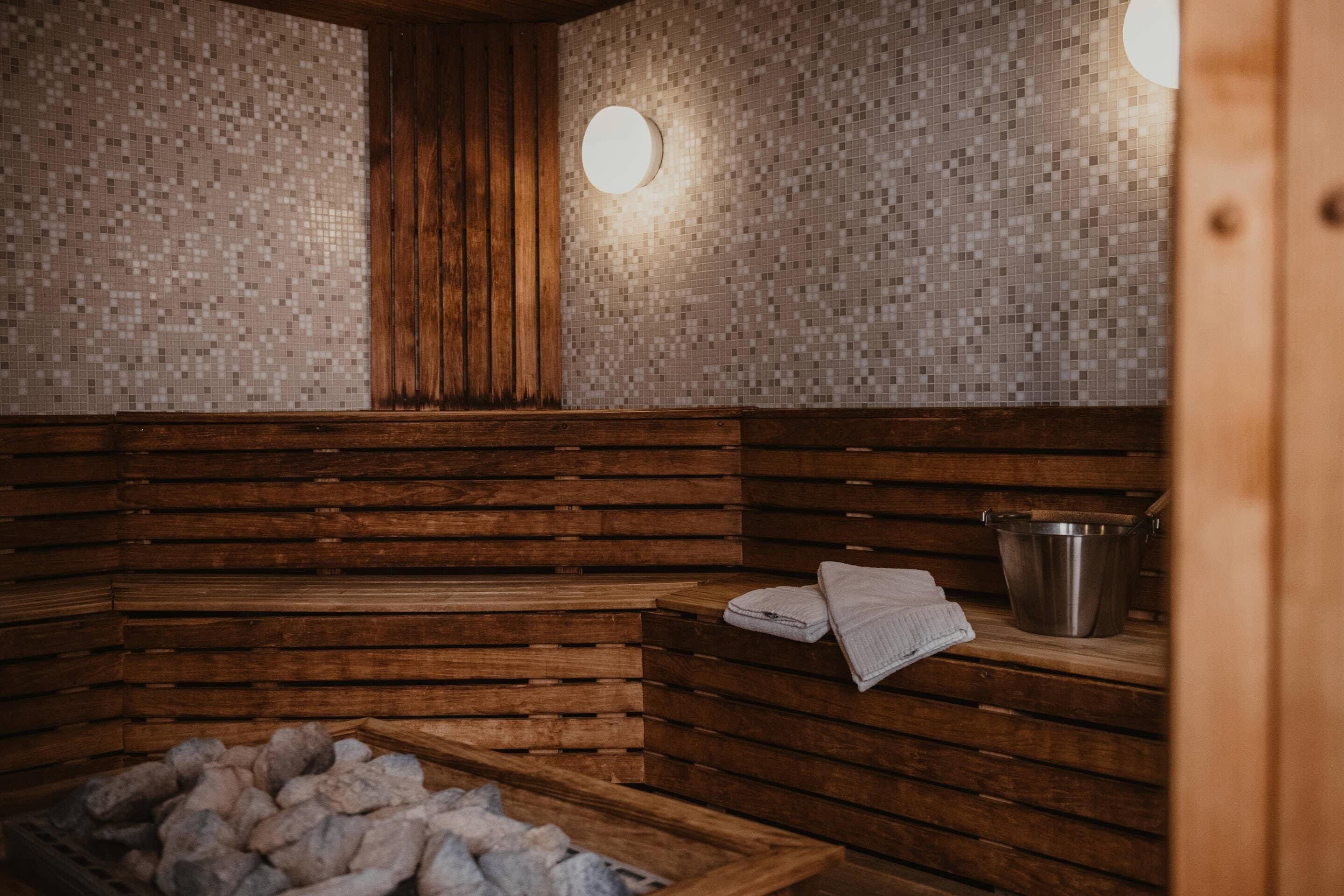 Una sauna con bancos de madera, una pila de piedra y un cubo de metal.