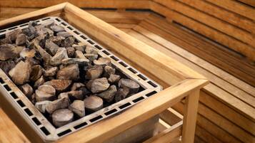 Uma sauna com um banco de madeira e uma grade de metal cheia de lenha.