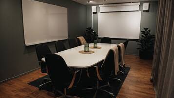 A conference room with a white table, black chairs, and two whiteboards on the walls.