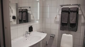 Un baño moderno con un lavamanos blanco, un espejo y dos toallas colgadas en un perchero.