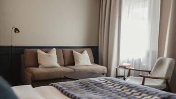 A hotel room with a bed, a sofa, a chair, a small table, and a lamp.
