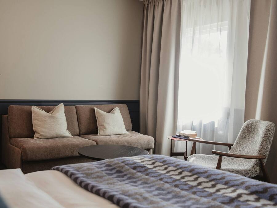 A hotel room with a bed, a sofa, a chair, a small table, and a lamp.