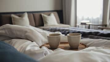 Una cama bien hecha con dos tazas de cerámica sobre una bandeja de madera, un cabecero y una ventana con cortinas.