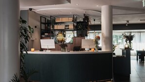 A reception area with a curved counter, shelves with various items, and potted plants. - Home Hotel Kompaniet (Nykoping)