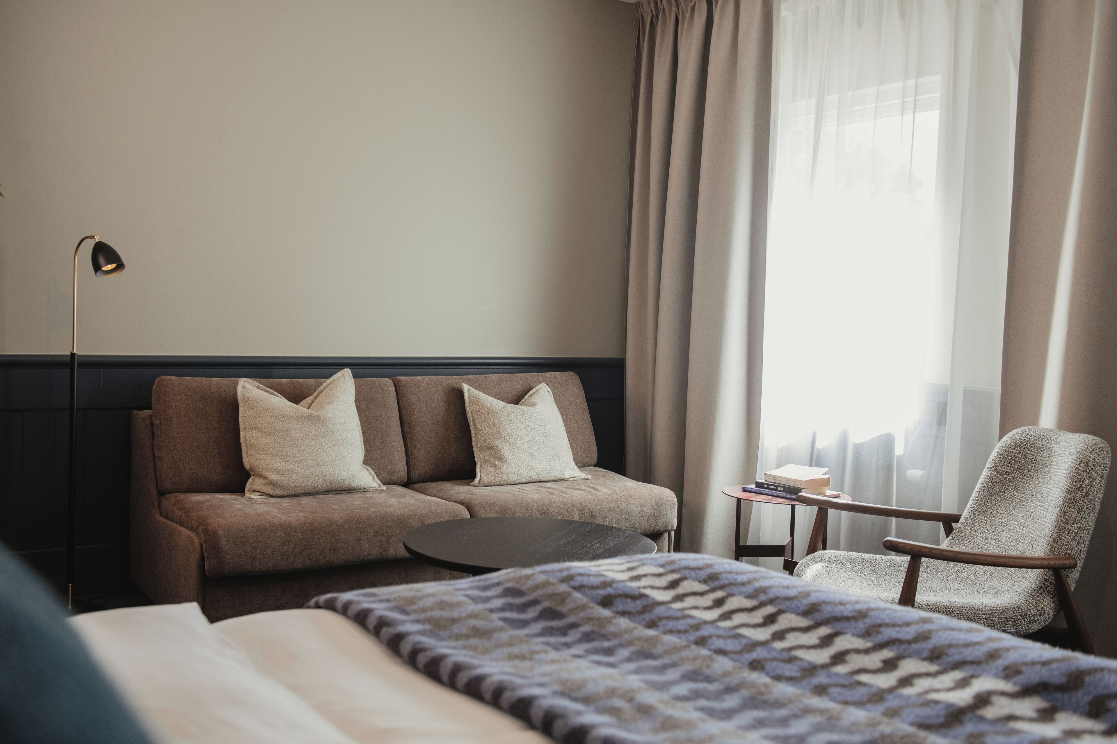 A hotel room with a bed, a sofa, a chair, a small table, and a lamp.