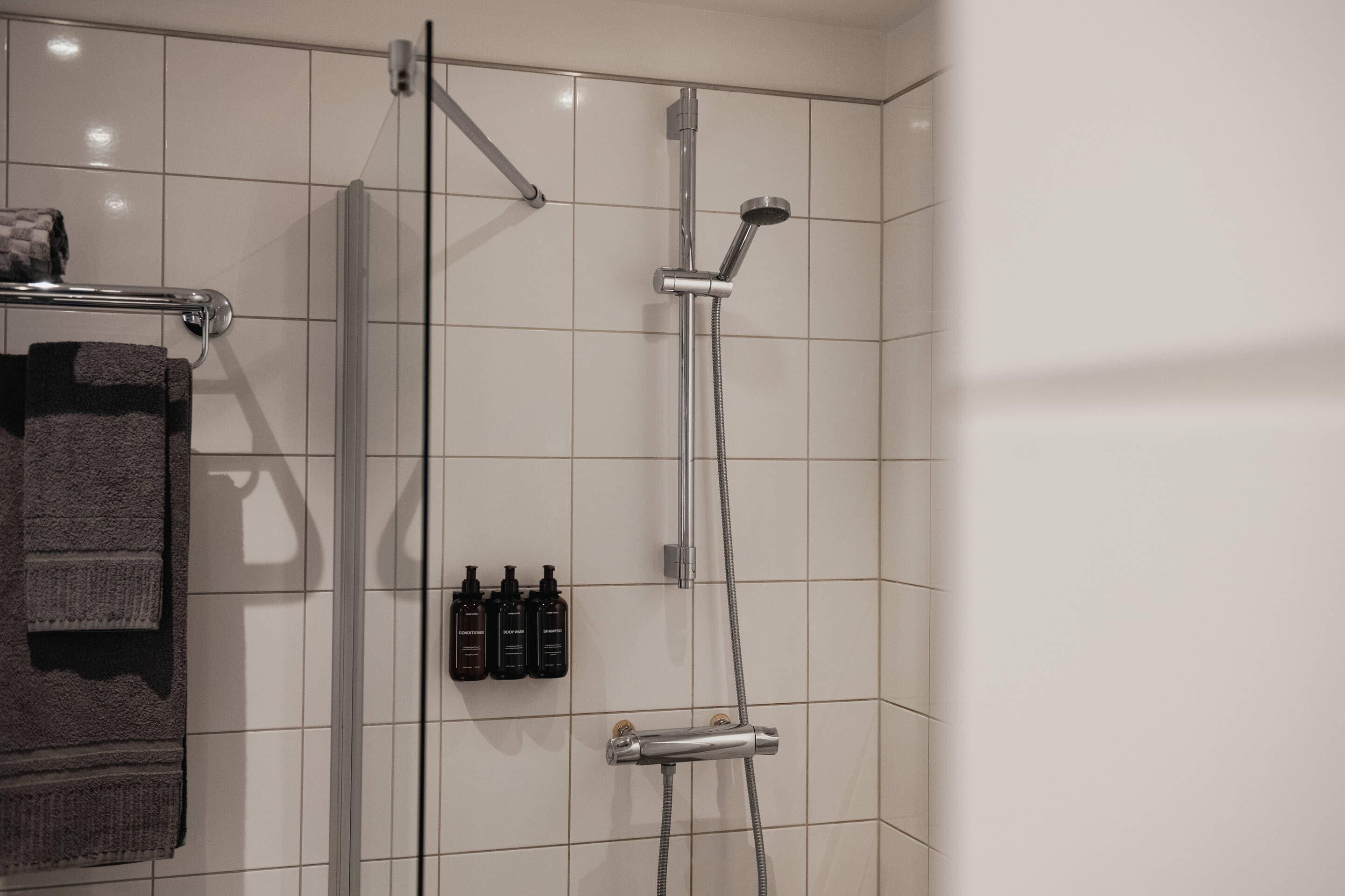 Un espace douche doté d’une porte en verre, d’un porte-serviettes avec une serviette, et de trois bouteilles de shampoing et d’après-shampoing.
