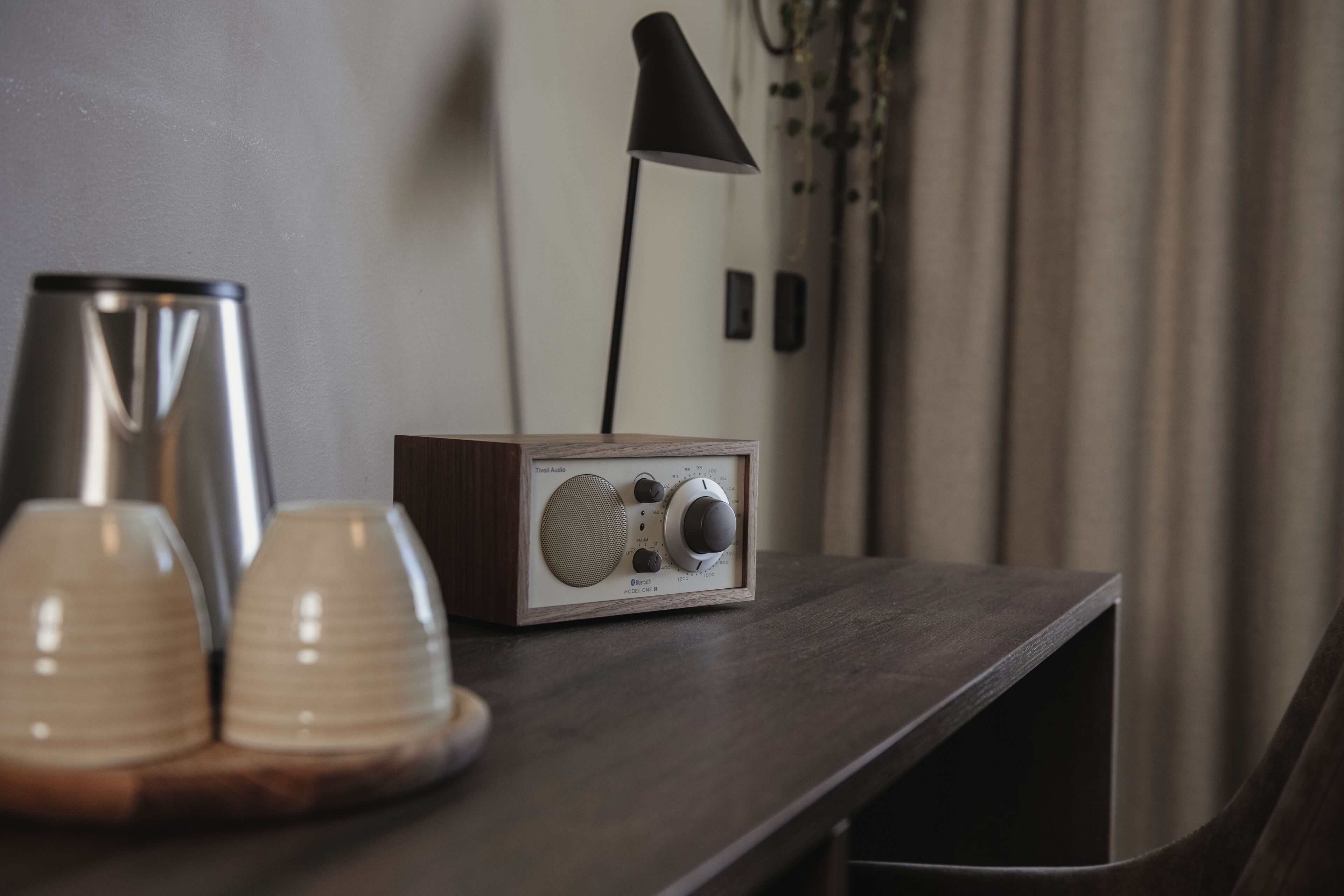 Uma mesa de madeira com um rádio, duas chávenas e um candeeiro.