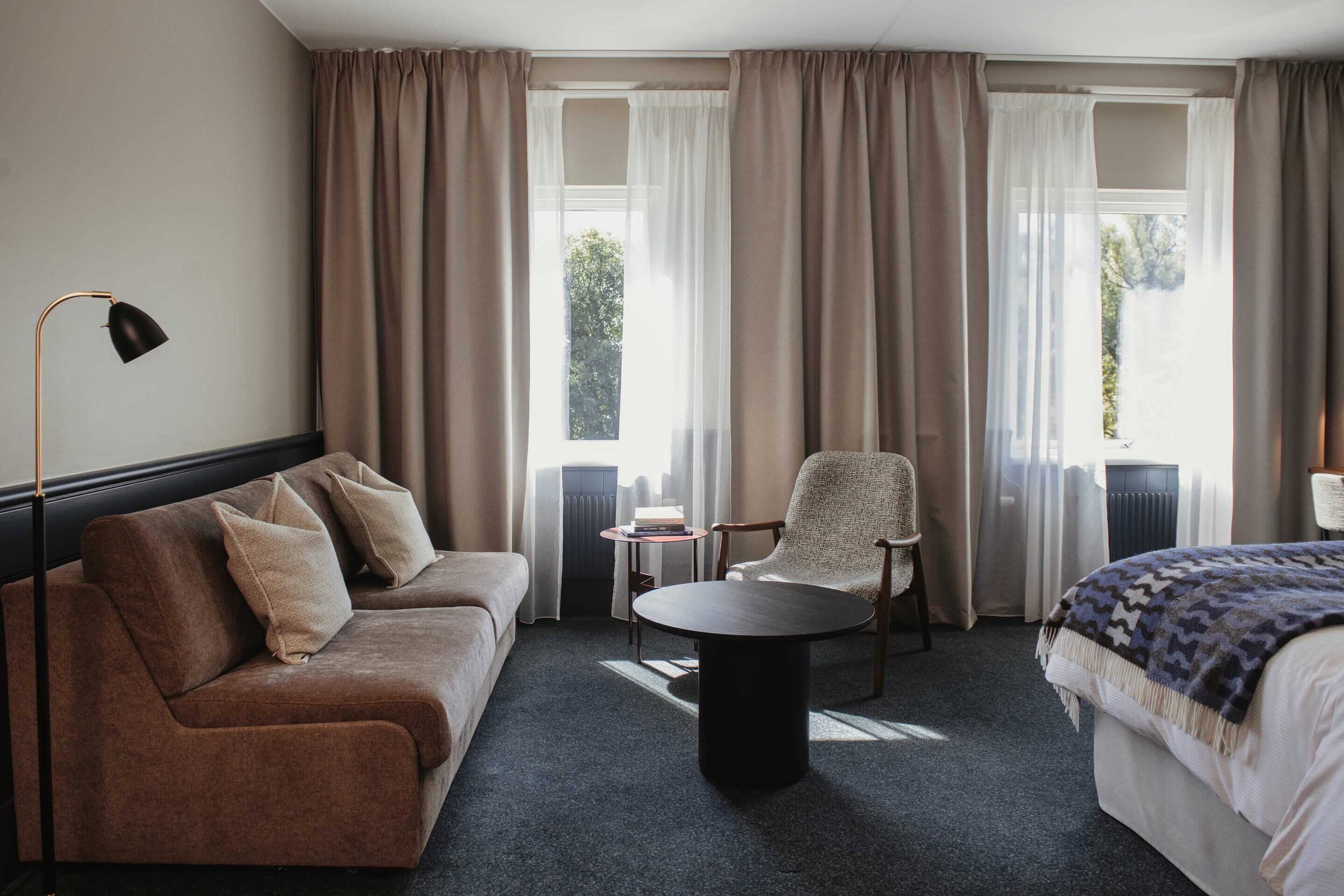 A hotel room with a sofa, armchair, round table, and a bed.
