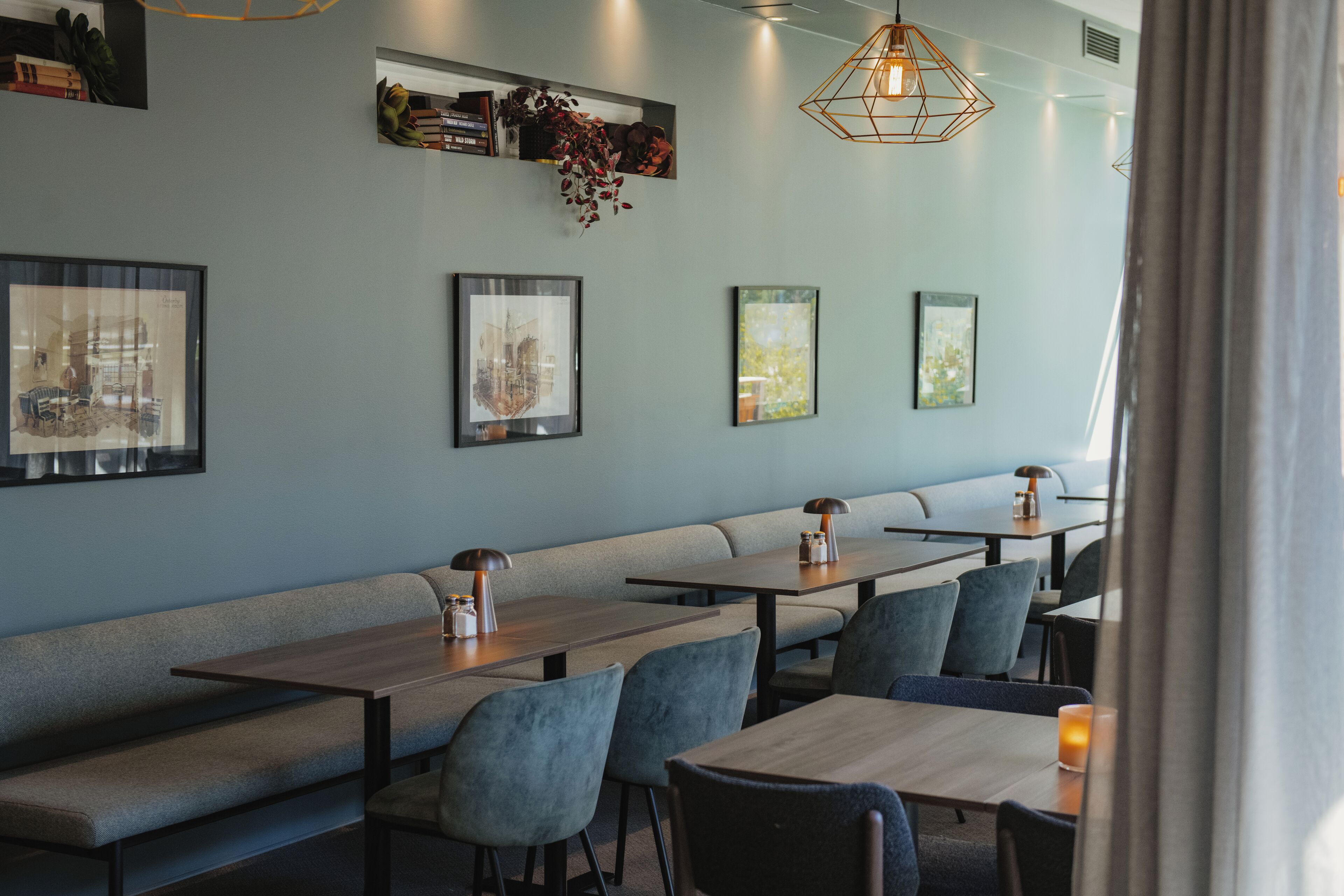 A restaurant interior with long communal tables, cushioned benches, and framed artwork on the walls.