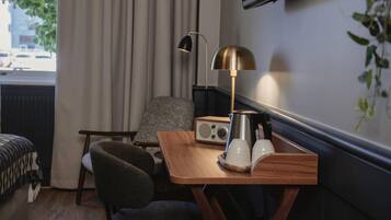 A hotel room with a wooden desk, a chair, a radio, a coffee pot, and a plant.