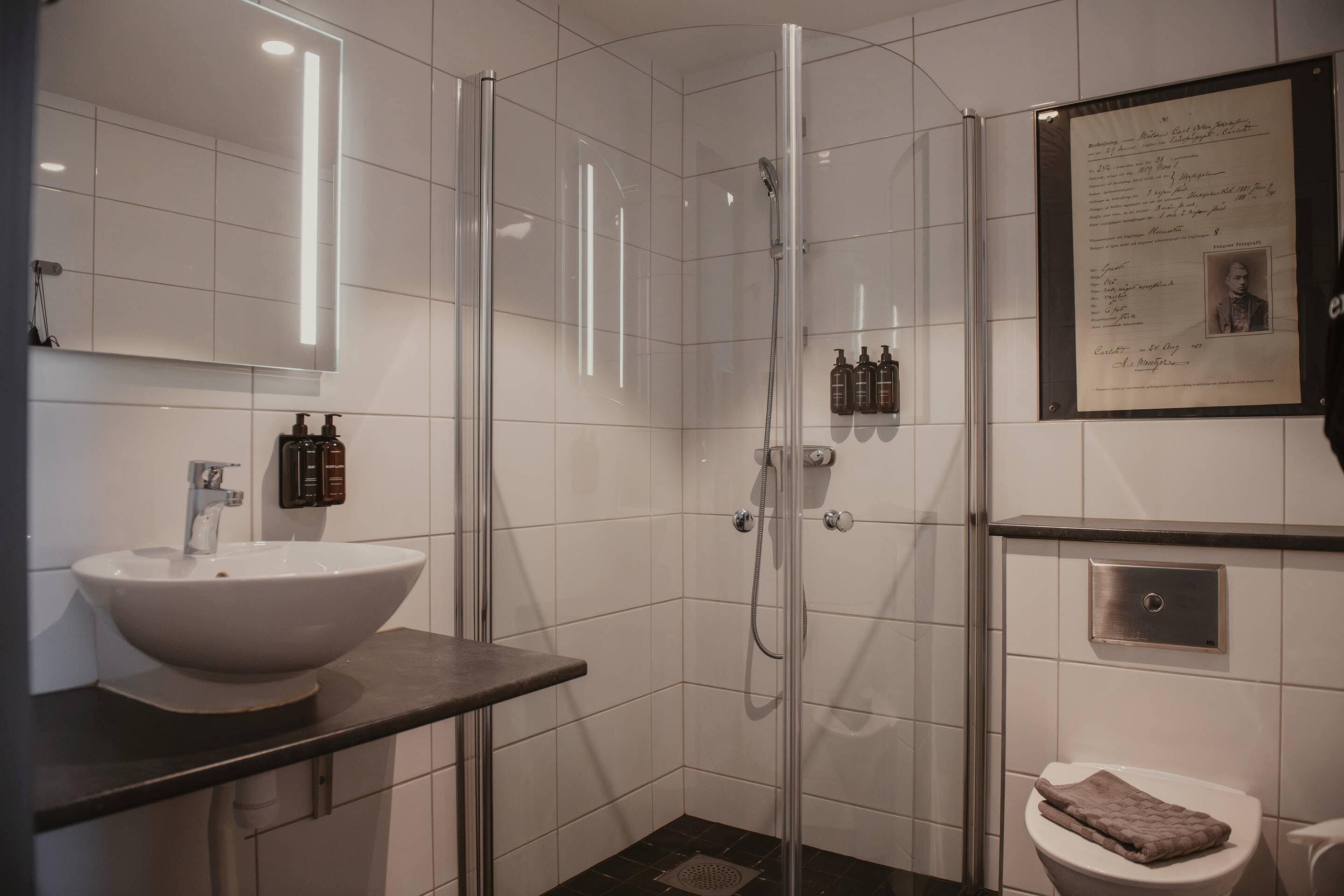 A modern bathroom with a glass-enclosed shower, a white sink, and a framed certificate on the wall.