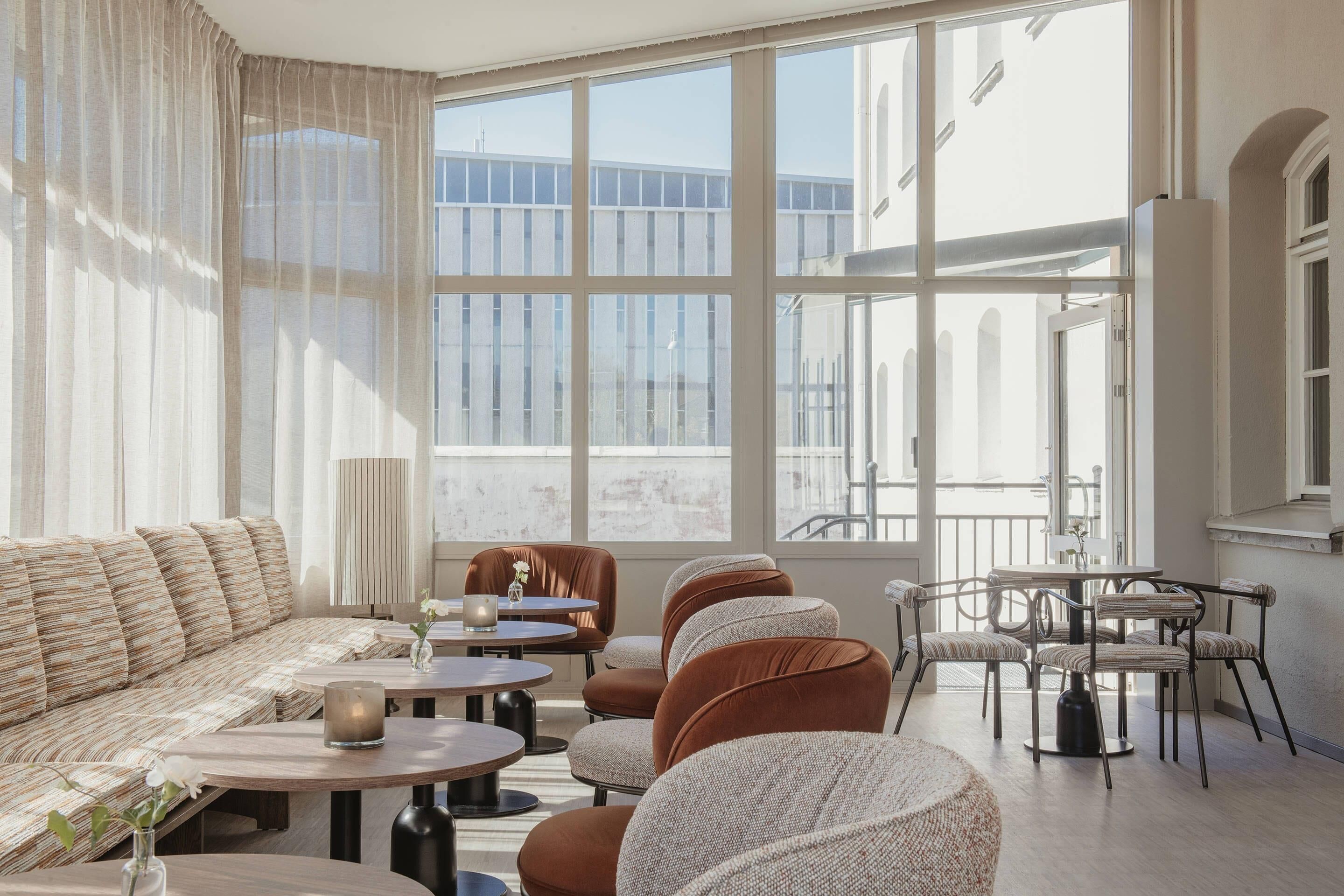 Ein modernes Interieur mit einer Couch, runden Tischen, Stühlen, großen Fenstern und Blick auf Gebäude.