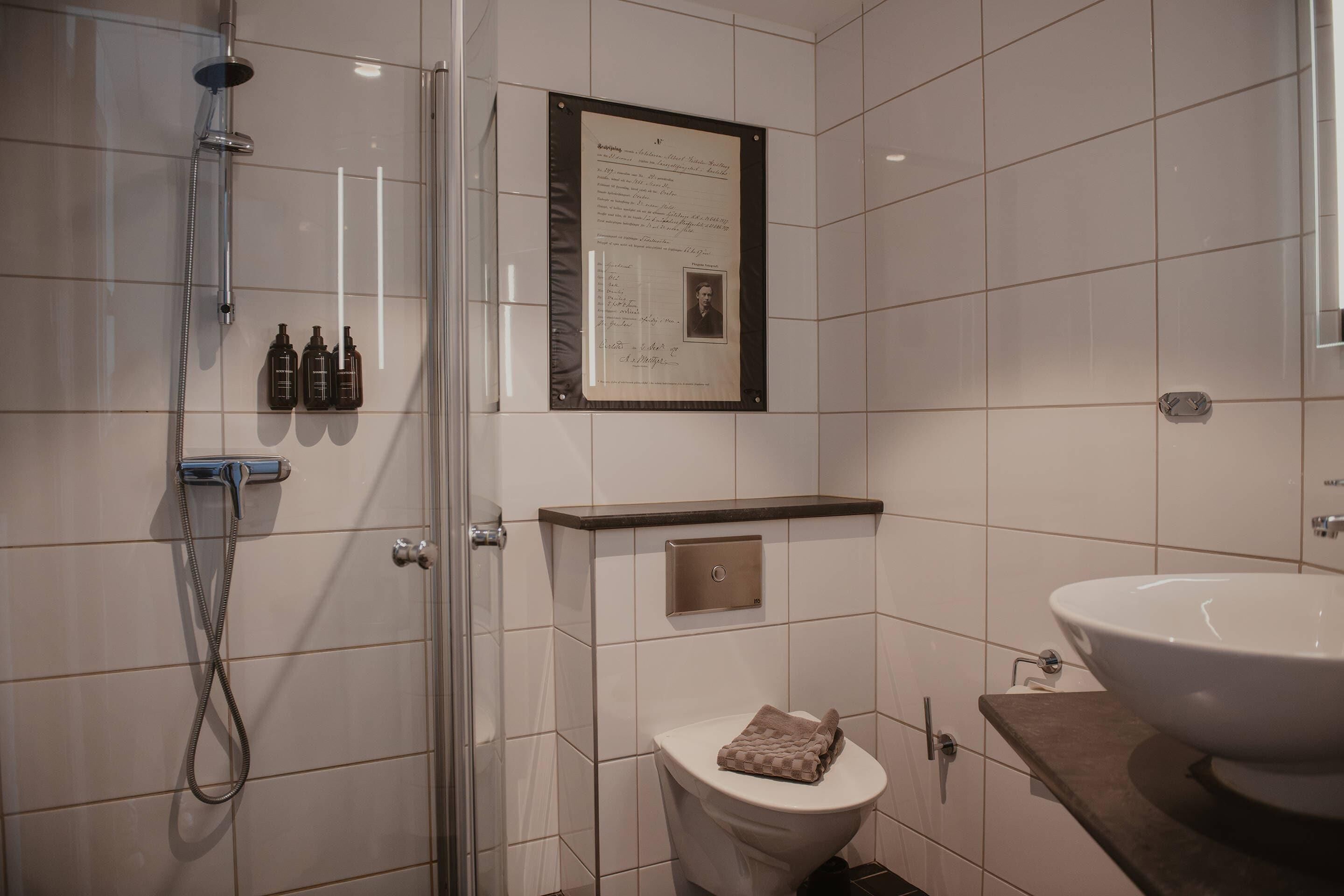 Un baño moderno con cabina de ducha de vidrio, un inodoro, un lavabo y un certificado enmarcado en la pared.