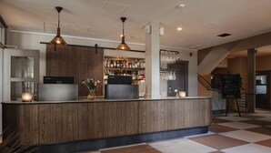 Zona de bar con mostrador de madera, iluminación colgante y una escalera al fondo.