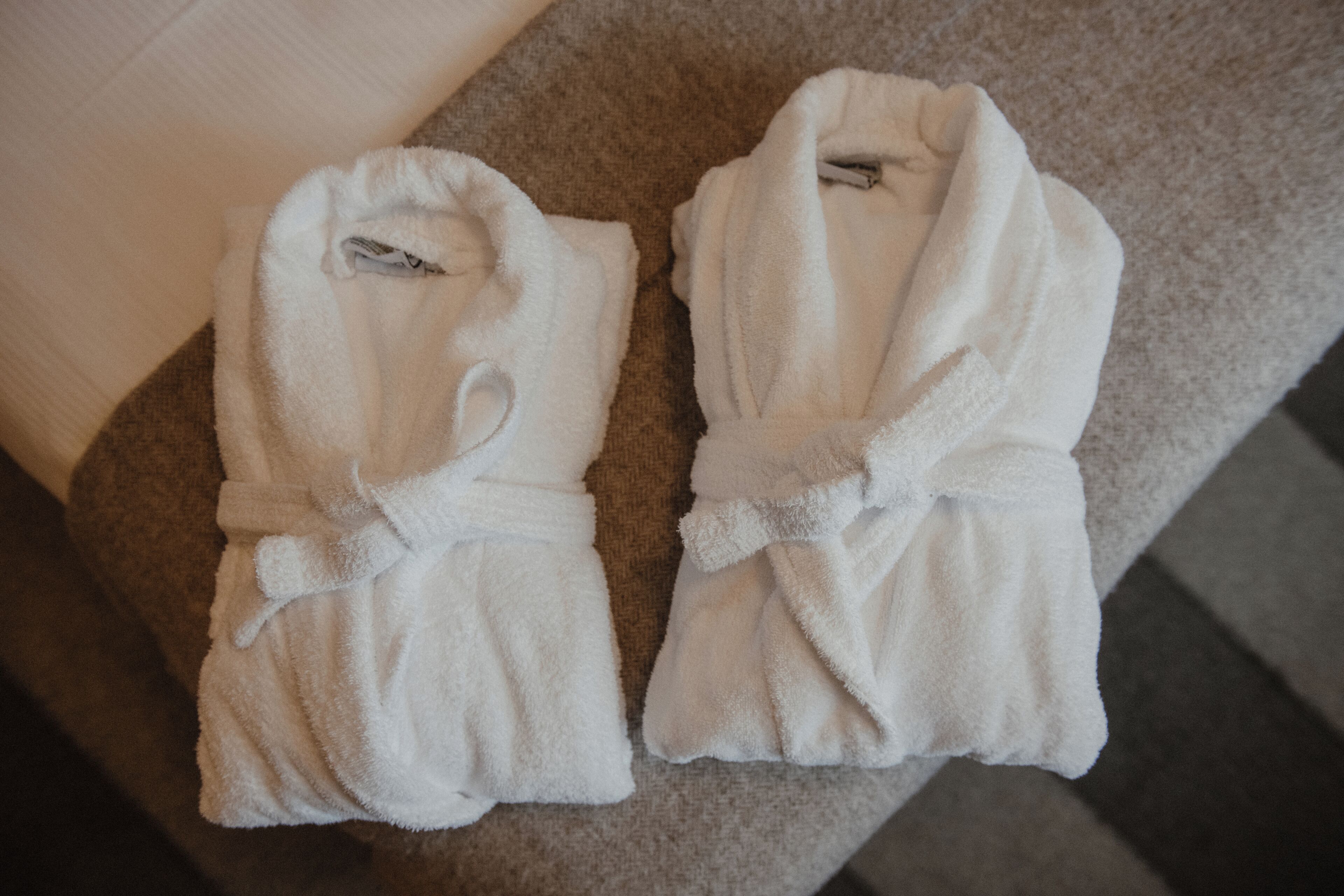 Two white bathrobes folded and placed on a beige carpeted surface.
