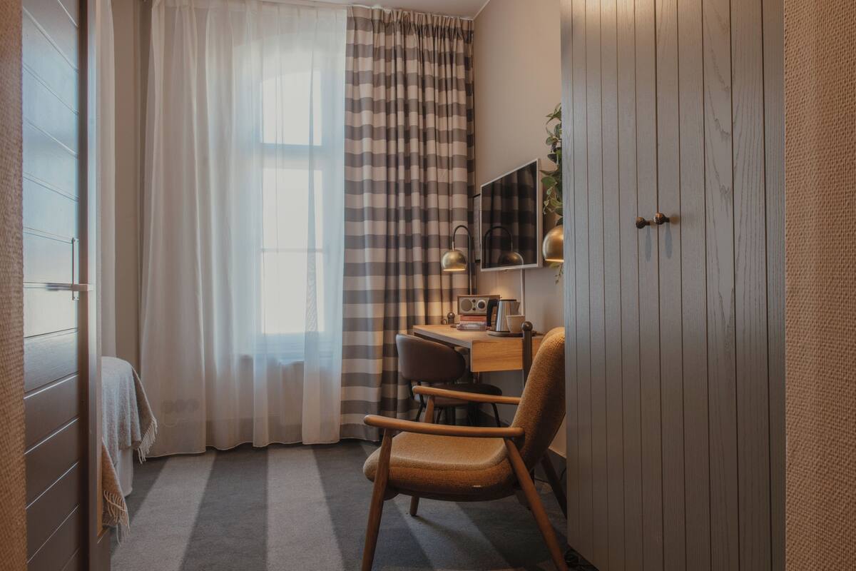 Una habitación de hotel con una cama, un escritorio con silla, una radio y un espejo en la pared.
