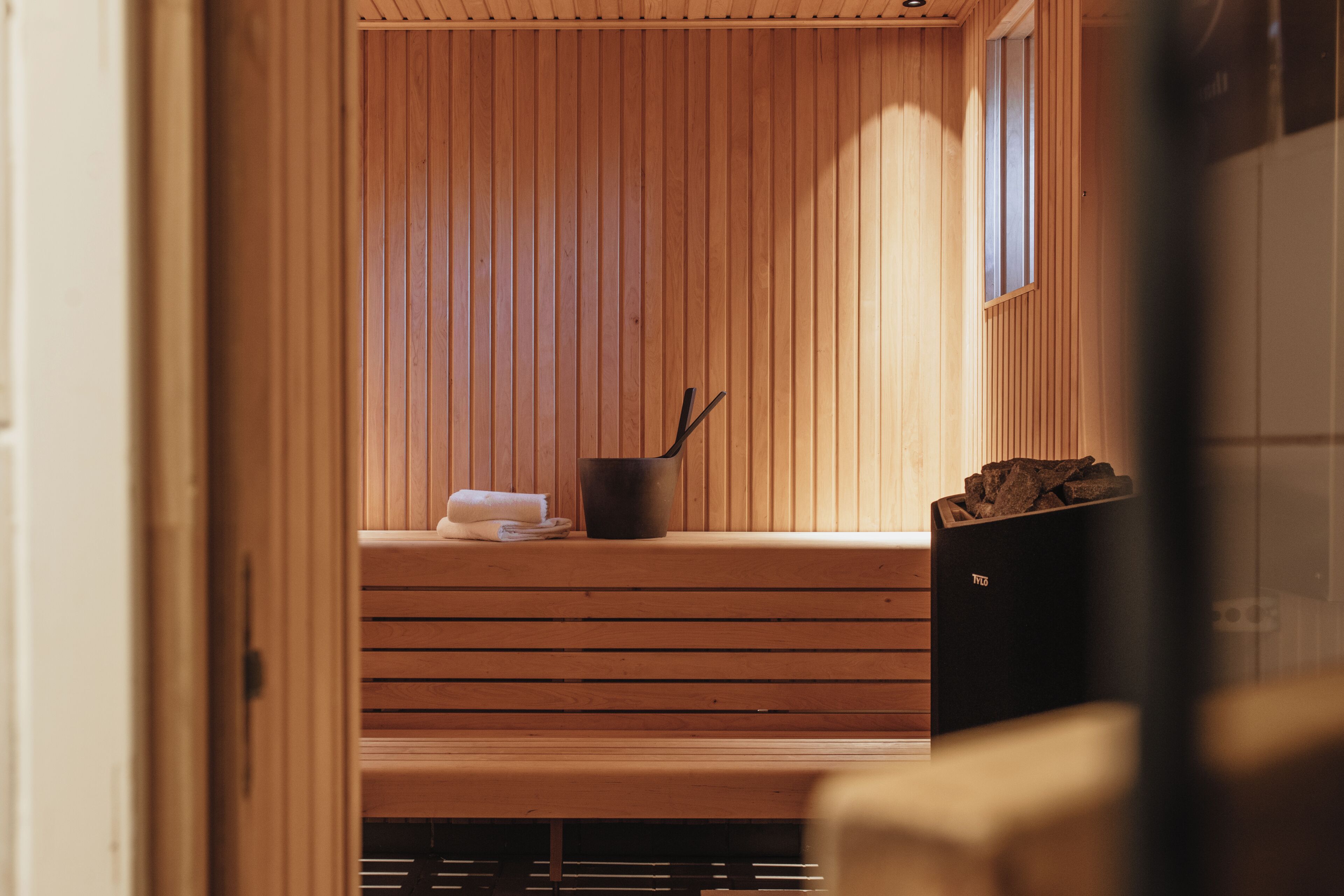 A wooden sauna with benches, a towel, and a bucket.