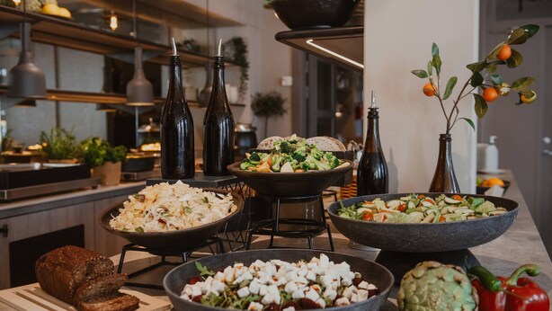 Una encimera de cocina con varios platos, incluyendo ensaladas, un bol de croutons y un alcachofa.