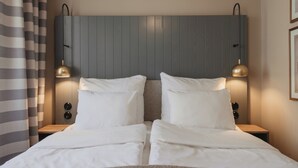 Una cama doble con cabecera, dos mesitas de noche y dos lámparas fijadas a la pared.