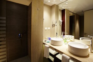 A modern bathroom with a large mirror, two sinks, a shower, and a towel rack.