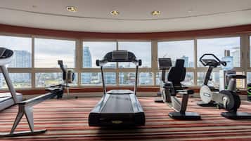 A fitness room with treadmills, ellipticals, and exercise bikes, large windows with a city view, and a red-striped carpet.